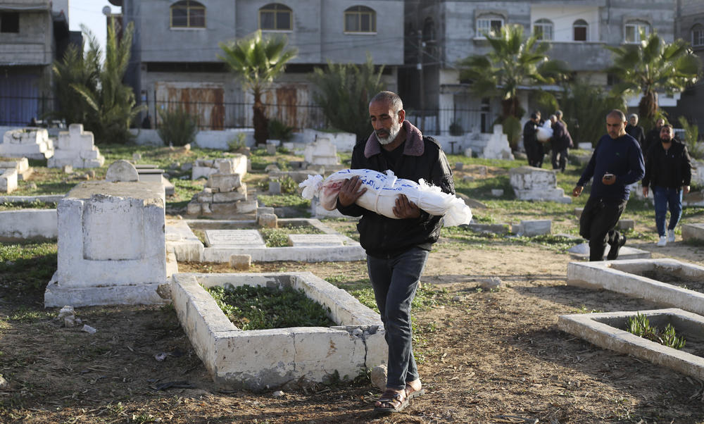 A Palestinian man carries a child for burial in the southern Gaza city of Rafah on Dec. 22. Israel's bombing campaign has killed more than 20,000 Palestinians in the territory,  most of them women and children, according to health officials in Gaza.
