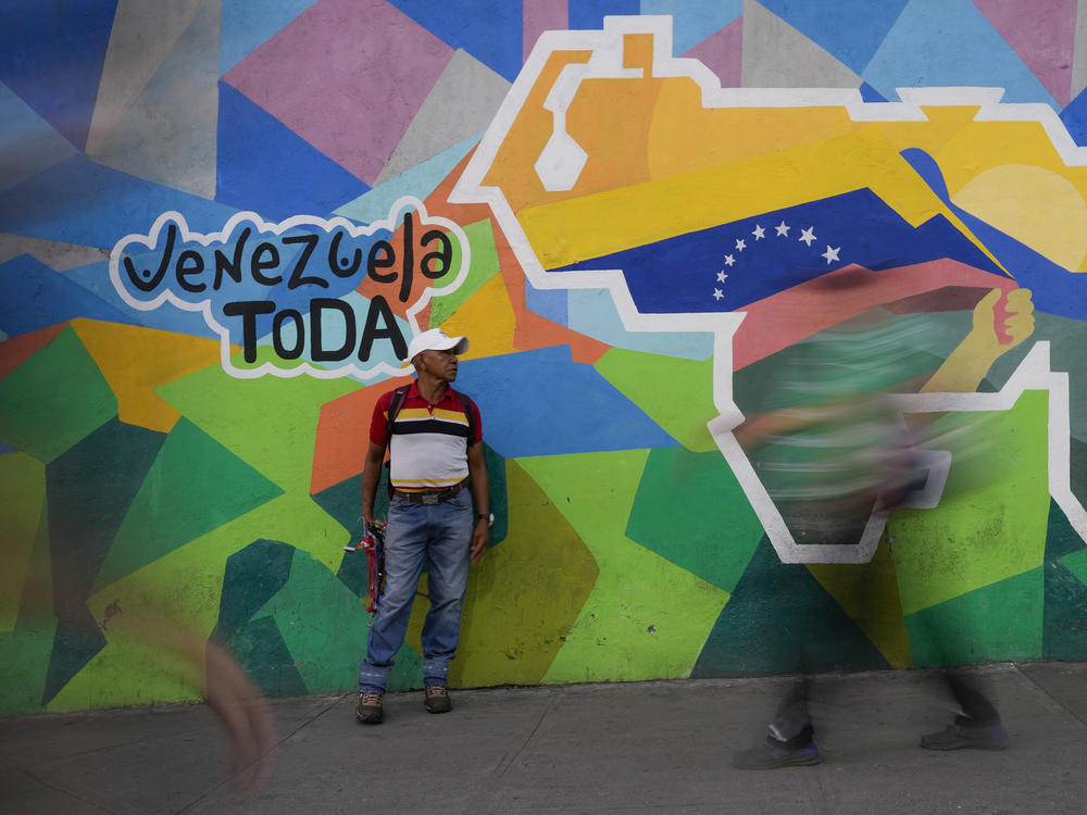 A man sells phone cables in front of a mural of the Venezuelan map with the Essequibo territory included in the Petare neighborhood of Caracas, Venezuela, on Dec. 11.