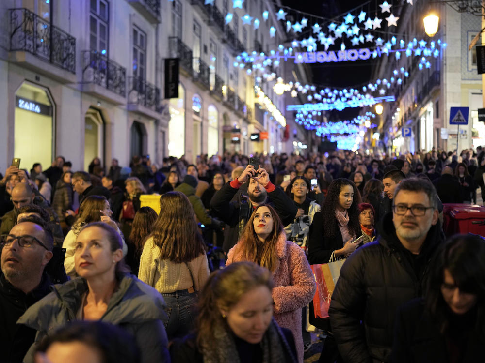 People look up at Christmas lights as crowds stroll around downtown Lisbon's Chiado neighborhood, on Saturday, Dec. 23, 2023.