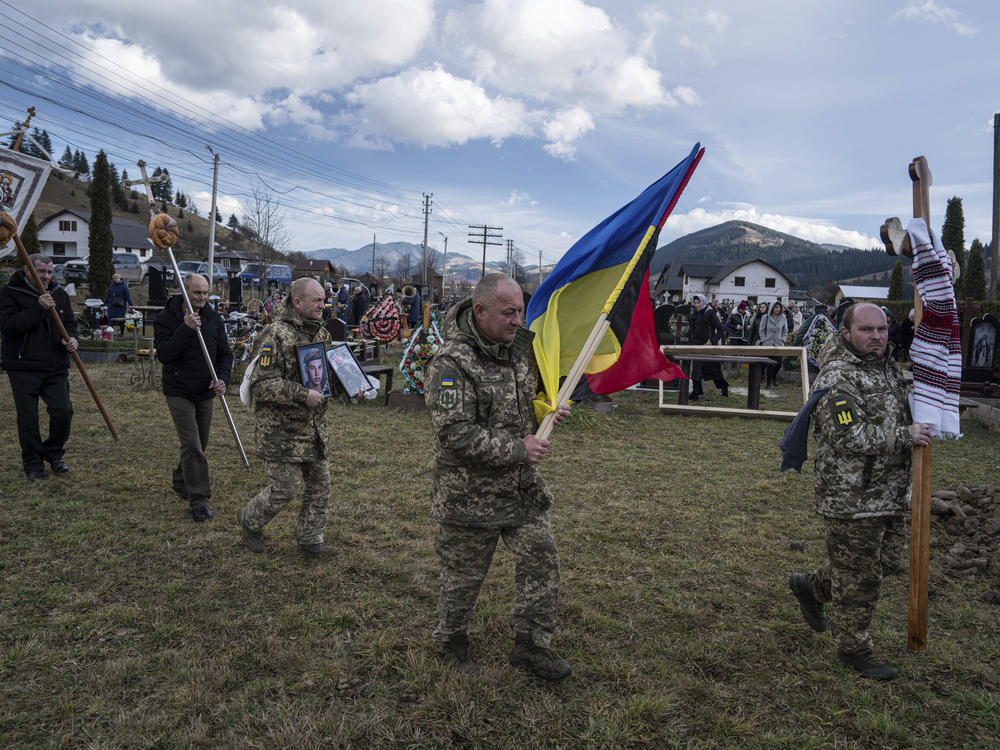 Ukrainian servicemen carry national flags and photos of their comrade Vasyl Boichuk, who was killed in Mykolayiv in March 2022, during his funeral ceremony at the cemetery in Iltsi village in Ukraine on Dec. 26, 2023.