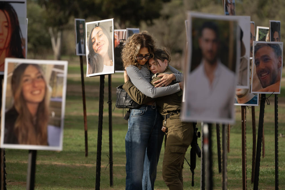 RE'IM, ISRAEL — Sigal Manzuri, whose daughters Norelle and Roya were killed in the Hamas-led attack on the Nova music festival on Oct. 7, embraces one of their friends. Surrounding them are photos of people killed and taken hostage by Hamas militants, displayed at the site as DJs spin music to commemorate victims. <a href=