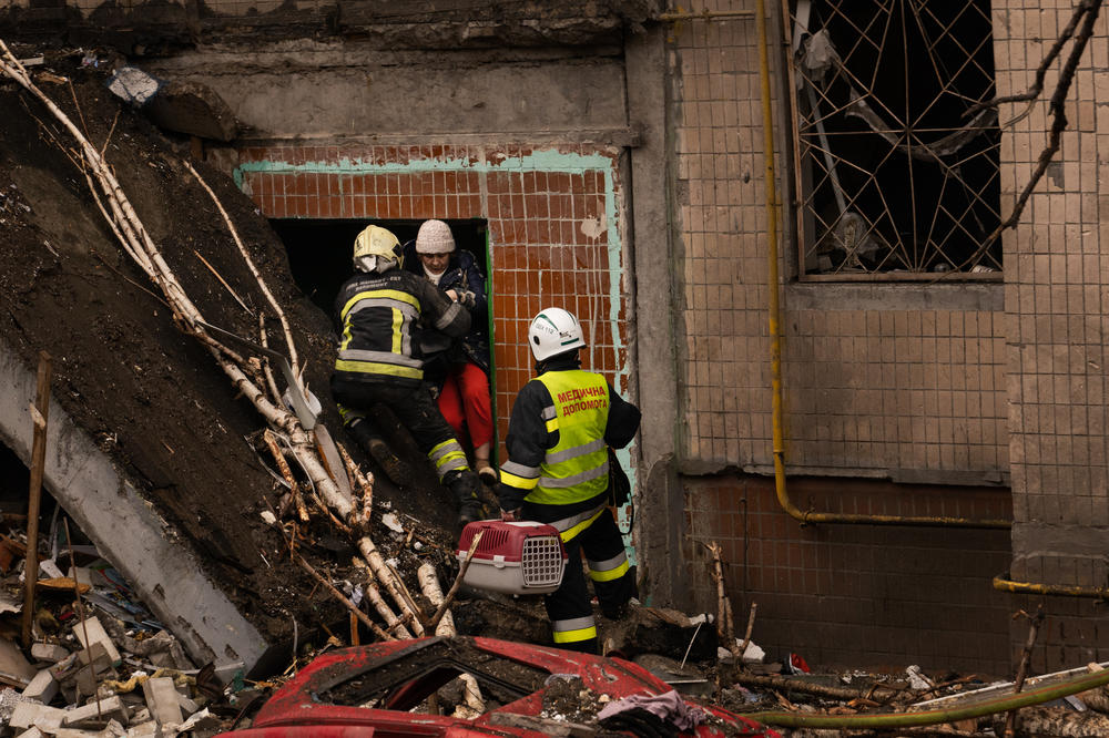Firefighters help a woman climb out of the building after she went inside to search for her cat, following the missile strike.