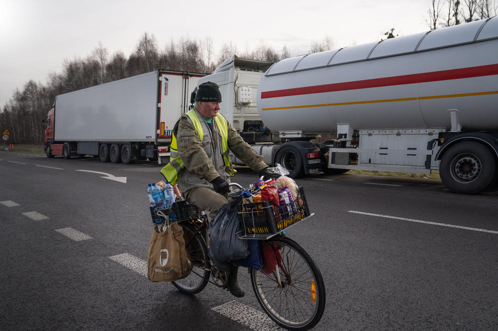 A man sells snacks and drinks from his bicycle to the Ukrainian truck drivers stuck at the border with Poland.