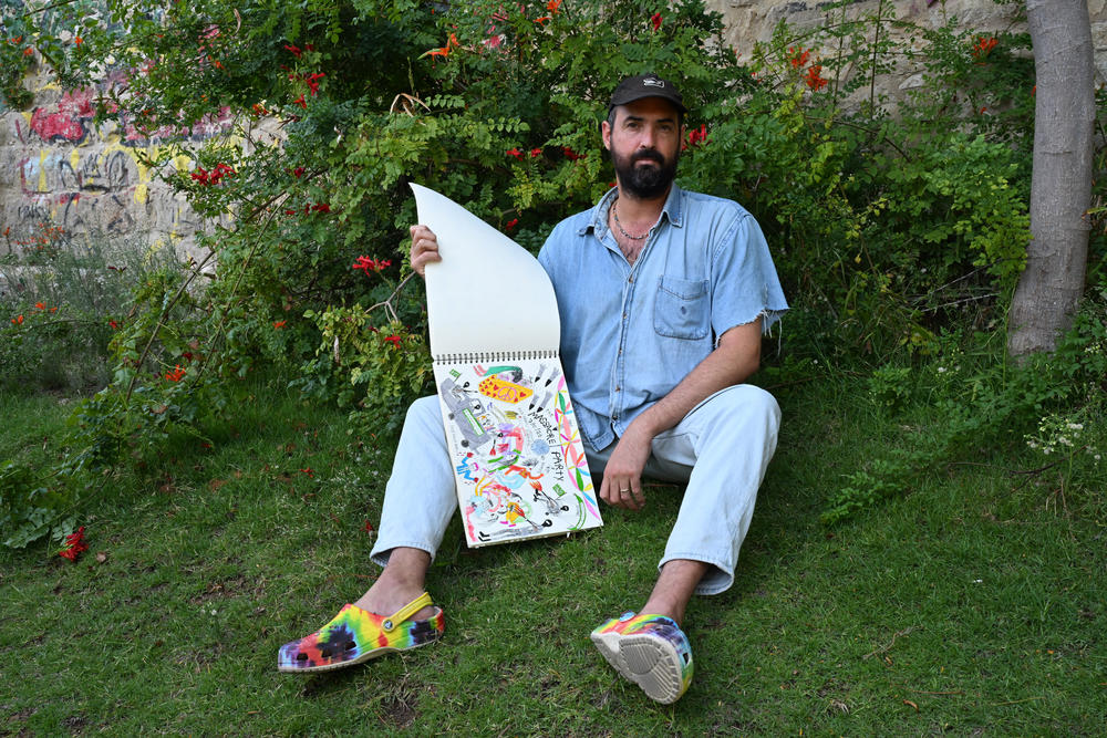 Oren Fischer—an Israeli artist—shares his sketch book in a park outside a cafe. He is from a kibbutz in the south of Israel, and creates political commentary on recent events.