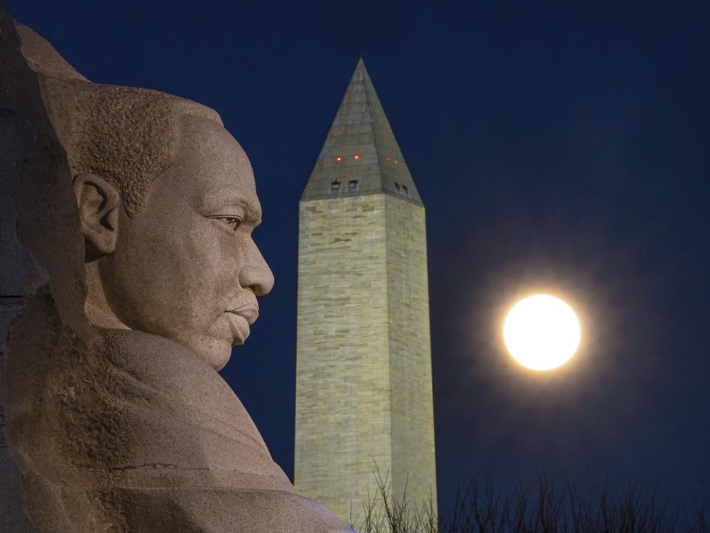 The rising full moon passes behind the Martin Luther King Memorial and the Washington Monument. MLK Day is the only federal holiday dedicated to volunteer service.