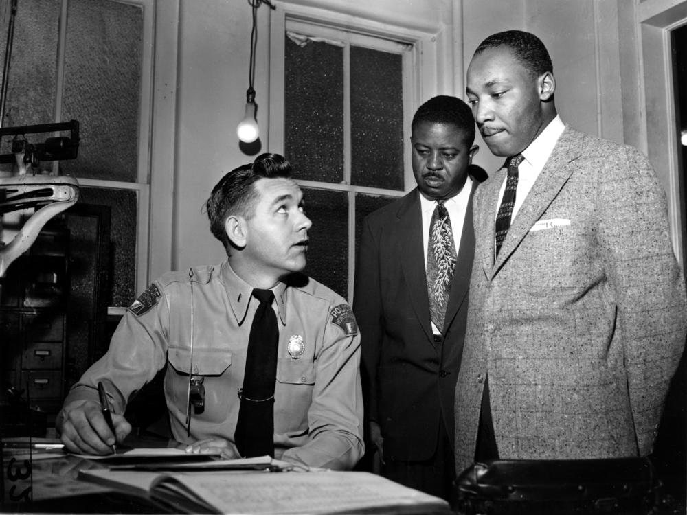 The Rev. Martin Luther King Jr., accompanied by Rev. Ralph D. Abernathy (center), is booked by city police Lt. D.H. Lackey in Montgomery, Ala., on Feb. 23, 1956.