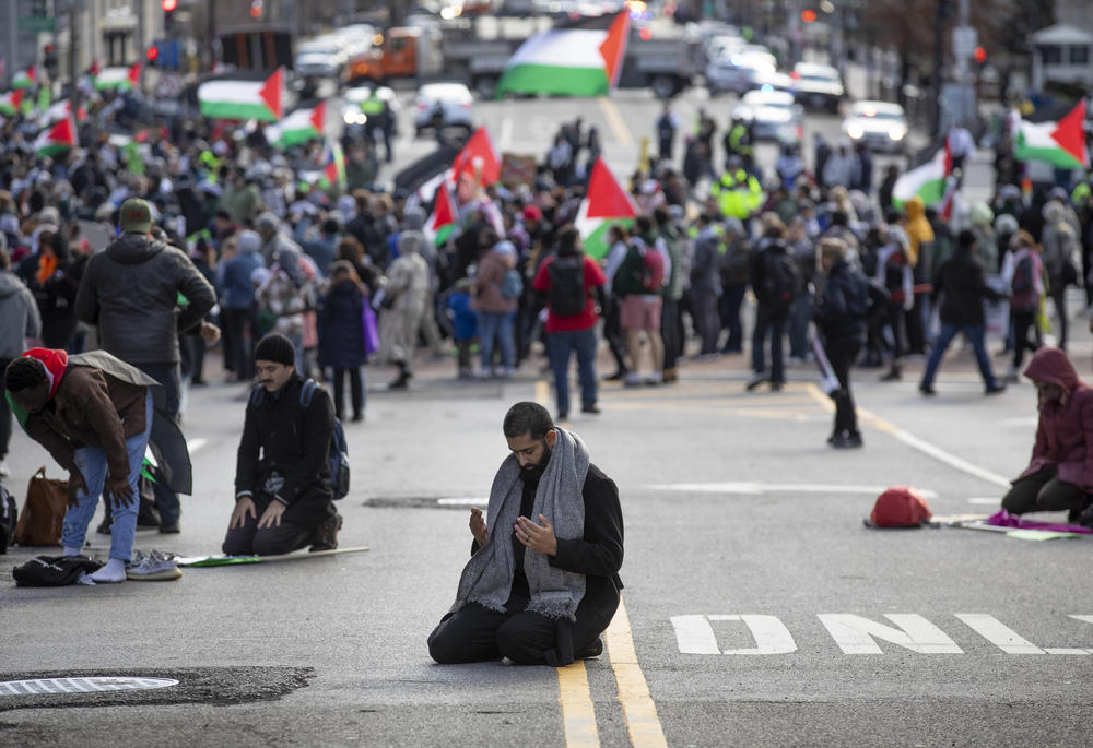 A person finishes his prayers on 14th Street as rally goers walk in the background.
