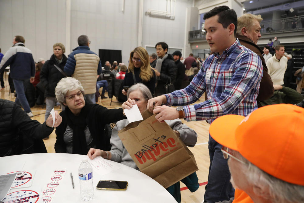 Voters dropping their ballots into a brown bag at a West Des Moines caucus site on Jan. 15, 2024.