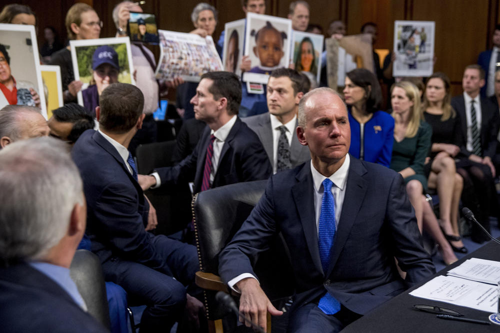 Then-Boeing CEO Dennis Muilenburg (center foreground) prepares to testify during an Oct. 29, 2019, hearing on Capitol Hill as family members hold up photographs of those killed in the Ethiopian Airlines Flight 302 and Lion Air Flight 610 crashes.