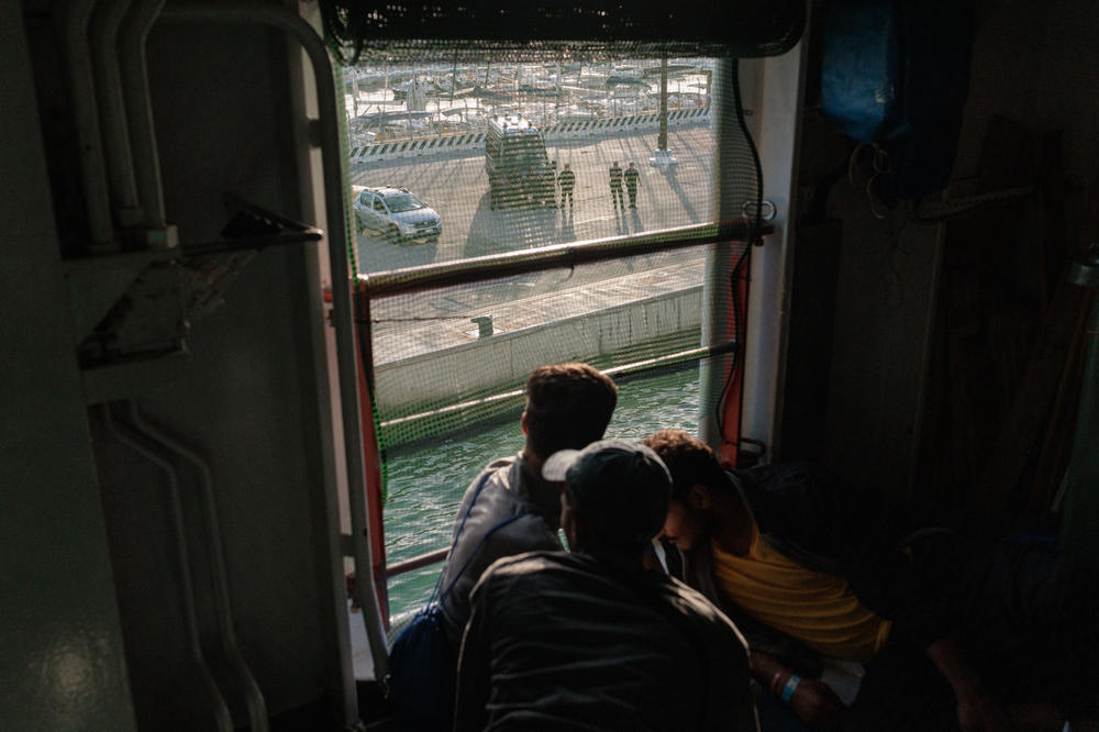 Migrants rescued by Doctors Without Borders observe police officers waiting on the dock at the port of Salerno, Italy.