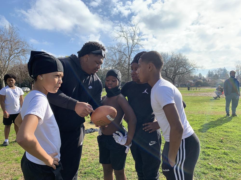 Daquan Williams, who coaches alongside Lorenzo Walsh, explains a potential play to (from left to right) Davon Martinez, Waylon Parker, Zakai Hood, and Kayden McLaughlin at a 7-on-7 practice at Tahoe Park in Sacramento, California on Jan. 14, 2023.