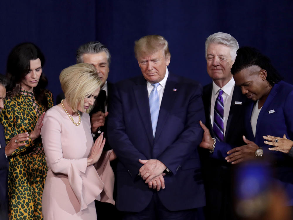 In this file photo from 2020, Pastor Paula White, left, and other faith leaders pray with President Donald Trump, center, during a rally for evangelical supporters at the King Jesus International Ministry church in Miami.