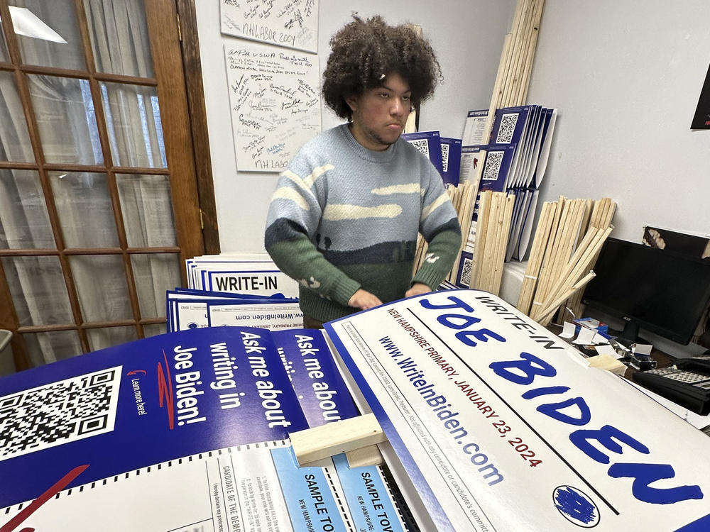 Malikiah Guillory, 19, stacks yard signs in Hooksett, N.H., on Wednesday, urging voters to write in President Biden's name on the Democratic primary ballot. Biden is skipping the New Hampshire primary because it didn't comply with party rules.