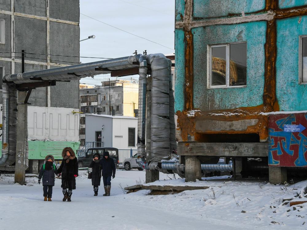 People walk next to a cracked panel apartment building in the eastern Siberian city of Yakutsk in 2018. Climate change is causing permafrost, or permanently frozen ground, to thaw across the Arctic. When the earth thaws, it can destabilize building foundations, roads, pipelines and other infrastructure.