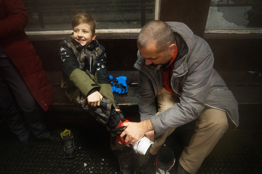 Nazar Motsia, 8, sits with his father, Maksym Motsia, who helps his son out of his gear after his first time skiing.
