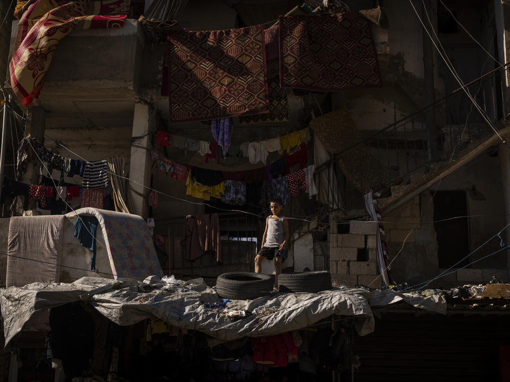 A Lebanese boy stands atop the roof of a crumbling house within the bustling streets of the Shatila refugee camp in Beirut.