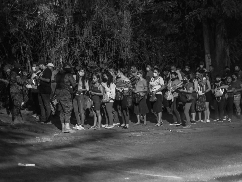 People line up to show their IDs to police at a checkpoint in Distrito Italia, a dangerous neighborhood in El Salvador, during the first days of the state of exception in April 2022.