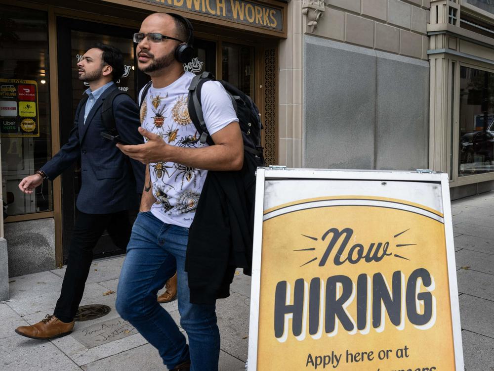 People walk past a hiring sign for a restaurant in Washington, D.C. on Oct. 5, 2023. A stronger-than-expected labor market has helped boost consumer spending.