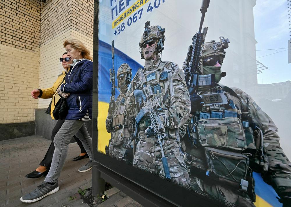 Pedestrians in Kyiv walk past a poster depicting Ukrainian servicemen and a slogan that reads, 