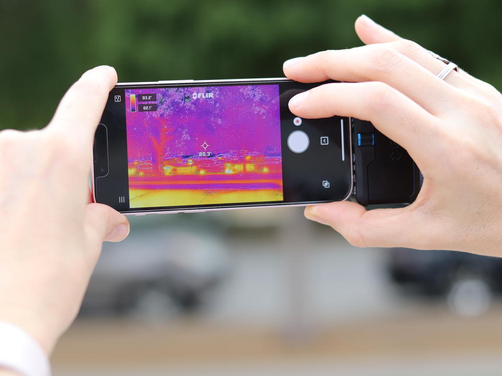 A thermal imaging device attached to an iPhone shows a range of temperatures with reds and oranges representing hot conditions. Some cities are mapping heat to better understand how to prepare for extreme temperatures.