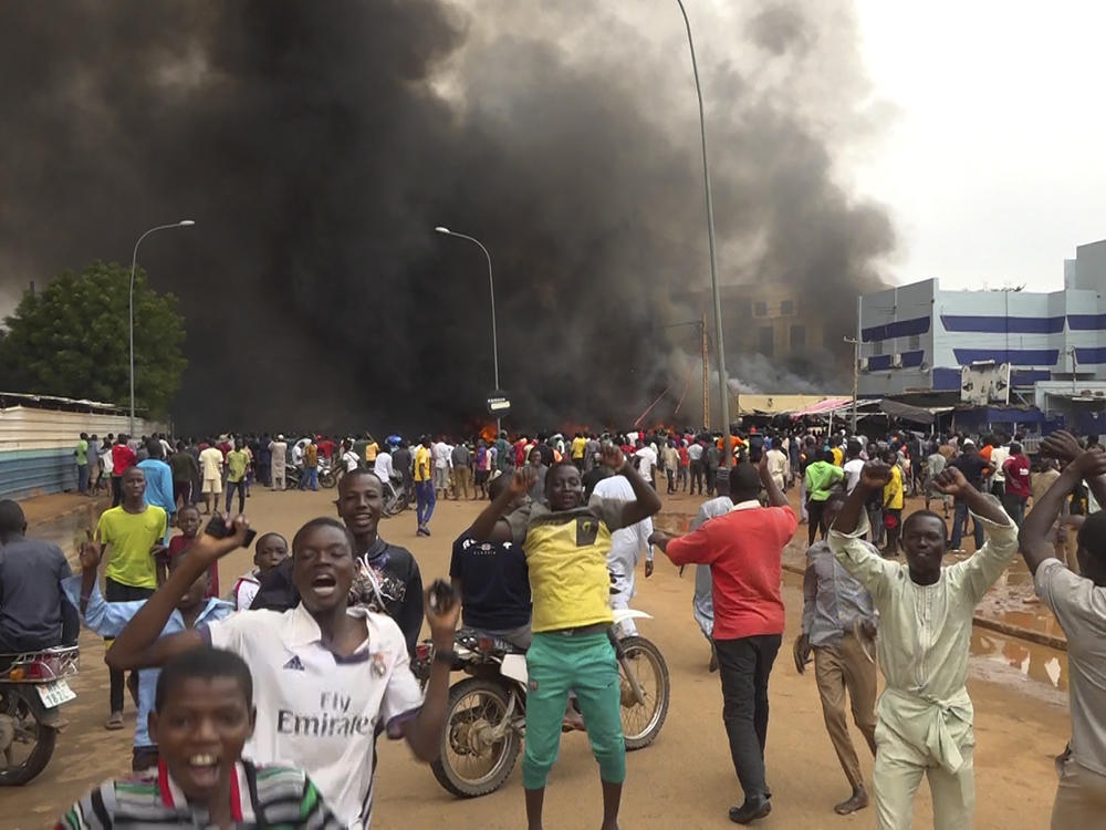 With the headquarters of the ruling party burning in the back, supporters of Niger's ruling junta demonstrate in Niamey, Niger, on July 27, 2023.