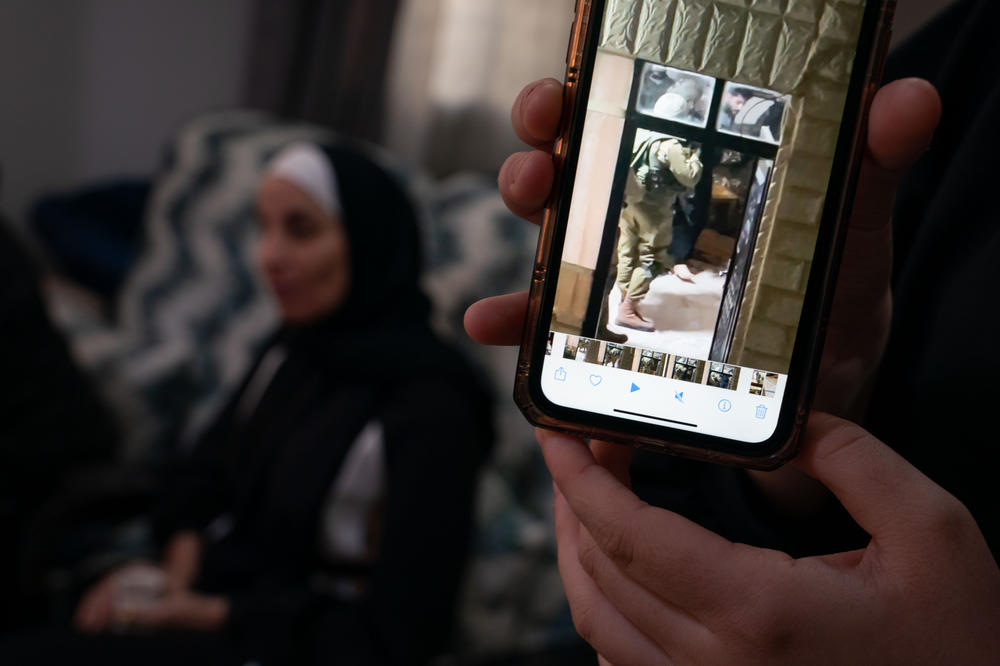 Deema Ali, 18, holds up her phone with an image of Israeli soldiers in their home during the arrest of her father Ala Al-Din Ali.