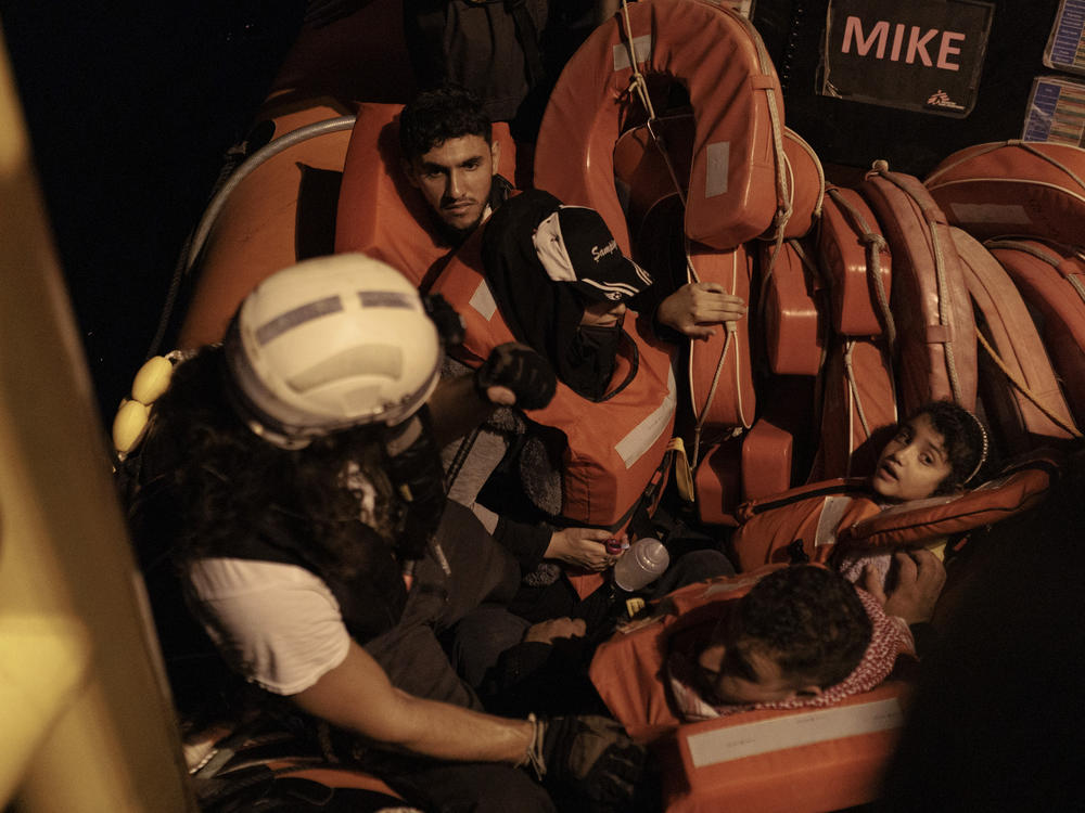 A rescue worker assists a Syrian family as they disembark from an inflatable boat. The family traveled with 158 other people on a wooden vessel that departed from Zawiya, Libya, at 8 p.m. the night before.