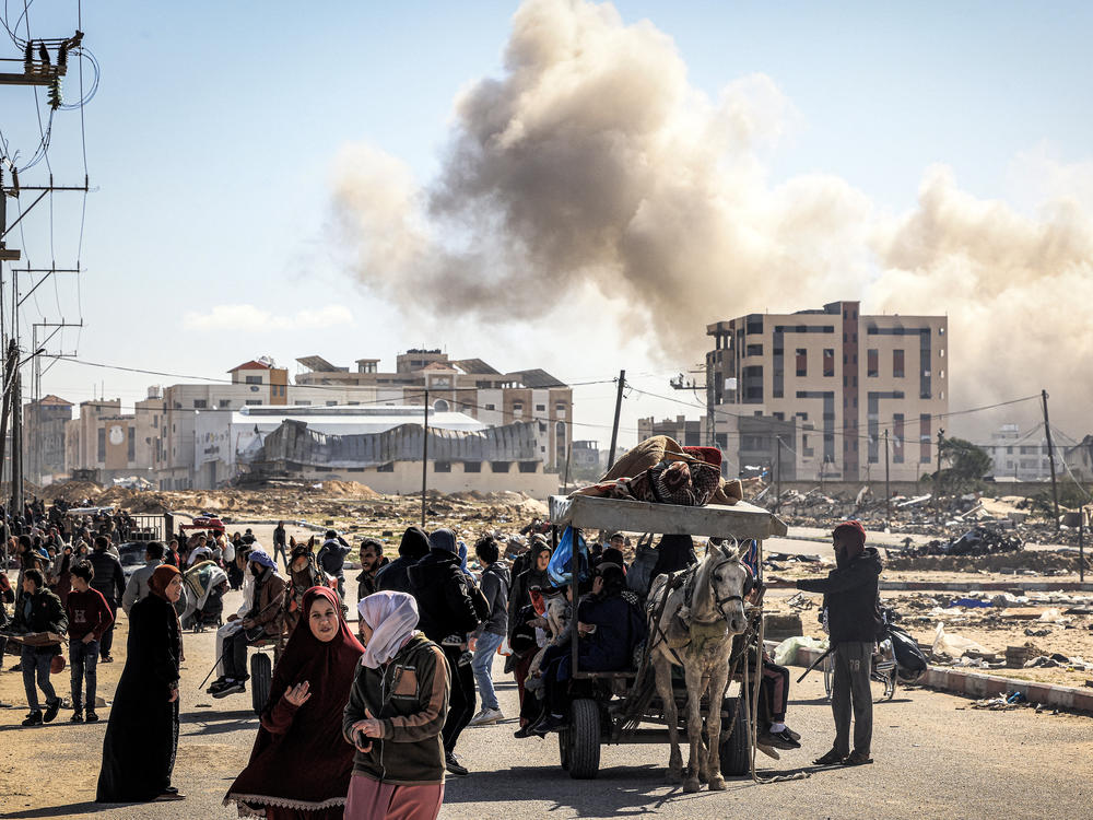 Smoke from a bombardment billows in the background as displaced Palestinians flee from Khan Younis, in southern Gaza, on Tuesday, Jan. 30.