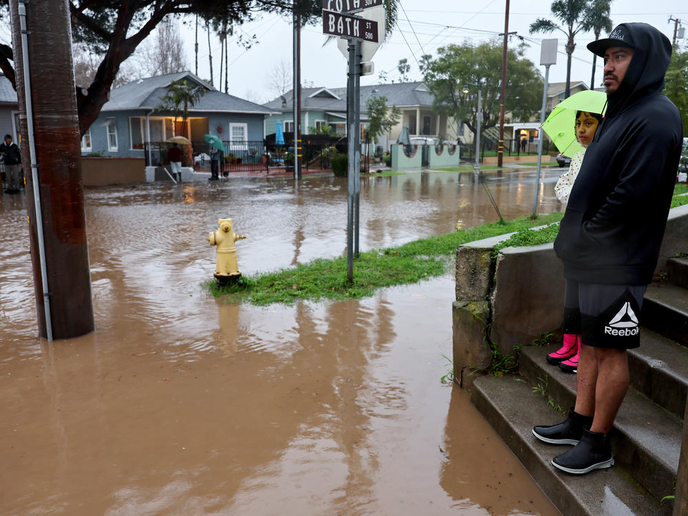Residents stand along a flooded street in Santa Barbara, California, as a powerful atmospheric river pummels the region. The storm has caused landslides, power outages, and road and airport closures across Southern California.