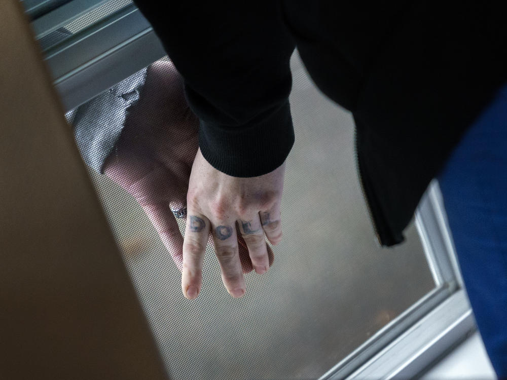 Unable to have visitors, Aleah and her boyfriend press their hands together, separated by the screen of an open window, as Aleah stays at Recovery Works Northwest's detox center.