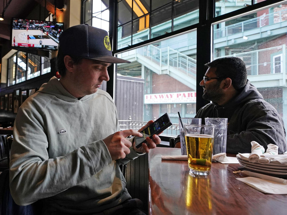 Taylor Foehl (left), of Boston, looks at a mobile betting app on his phone after placing a wager, while watching a men's college basketball game at the Cask 'N Flagon sports bar on March 10, 2023, near Fenway Park in Boston.