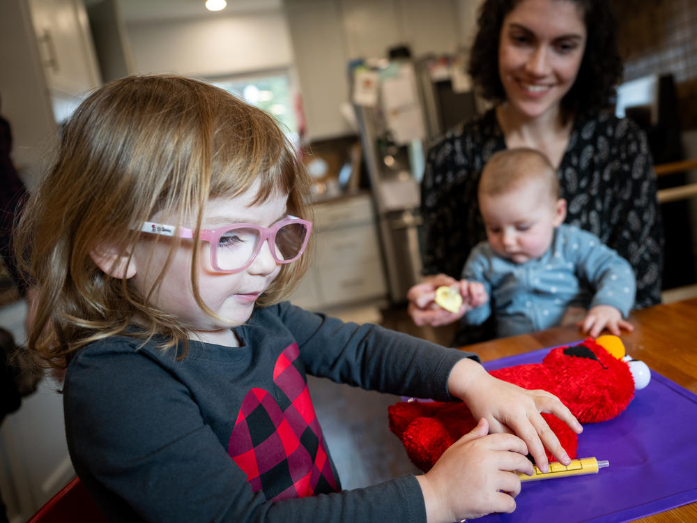 Julia Cramer sits with her two children, Maya, 3, and Lily, 6 months, at their home in Petaluma, Calif., on Dec. 19. Maya uses a toy medical syringe on an Elmo doll that she often brings along to the doctor's office.