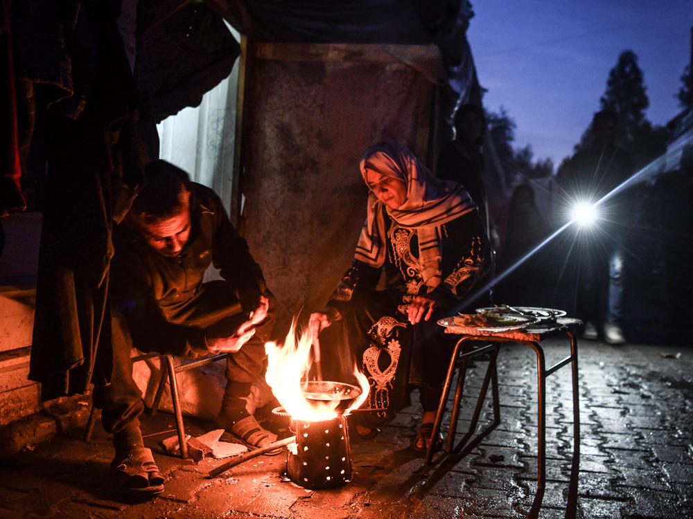 Palestinians who took refuge in schools amid ongoing attacks by Israeli forces try to stay warm and cook a meal on an open fire in the Rafah schoolyard on Thursday, Feb. 8.