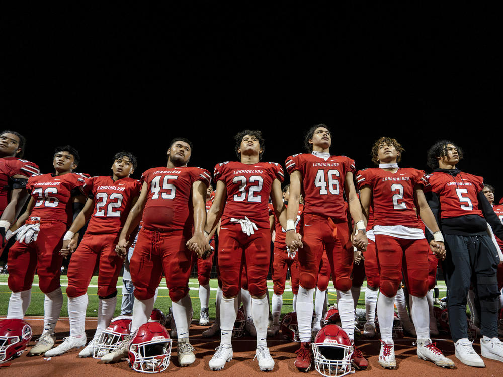 FILE - The Lahainaluna High School football team hold hands to thank the fans after a game on Oct. 21, 2023, in Lahaina, Hawaii. Captains of the team whose town was destroyed by a deadly wildfire attended to Super Bowl in Las Vegas as guests of the NFL.