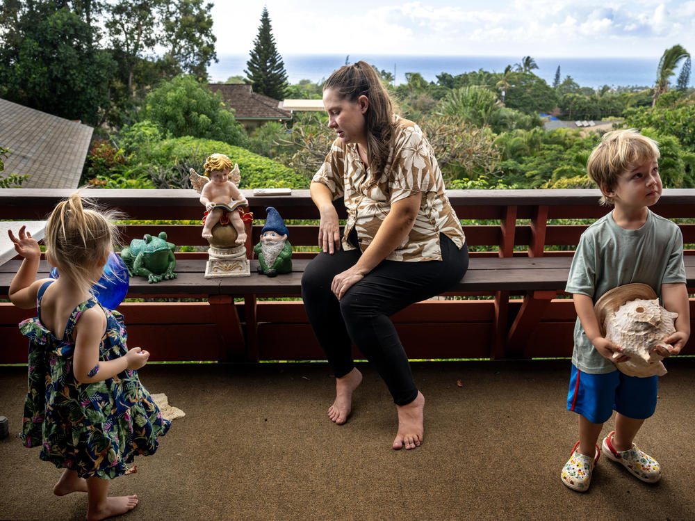 Arica Lynn Souza and her children Ayla, 3, left, and Silas, 4, on the porch of the family home where they are staying temporarily after losing their Lahaina townhome in the wildfires.
