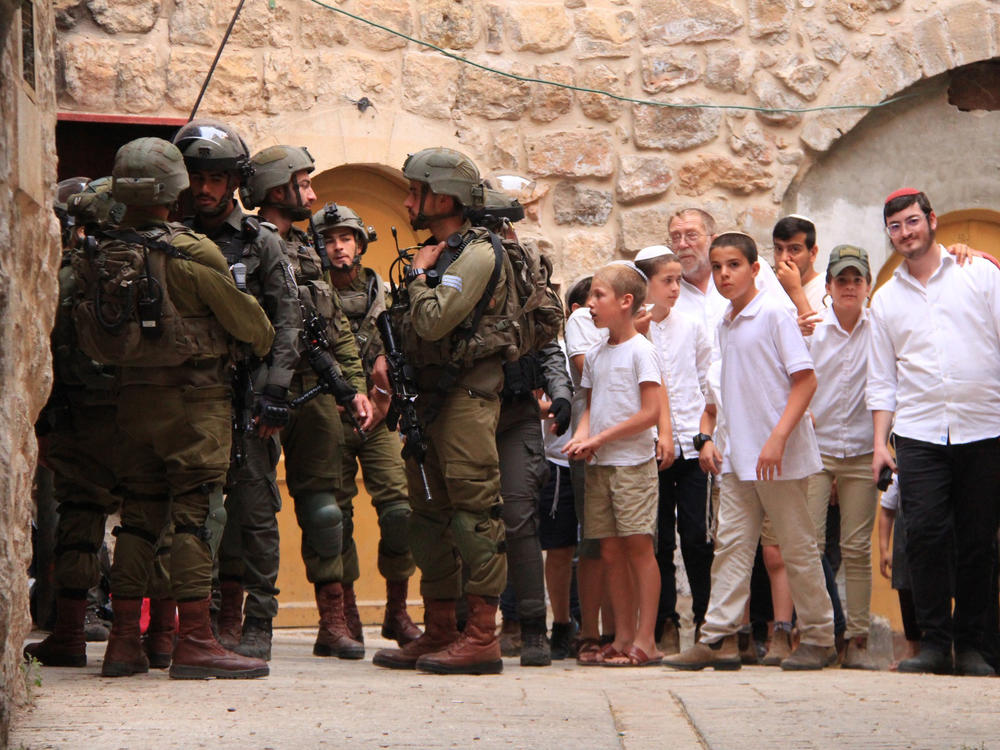 A group of Jewish settlers stands near Israeli soldiers in Hebron on May 27, 2023.