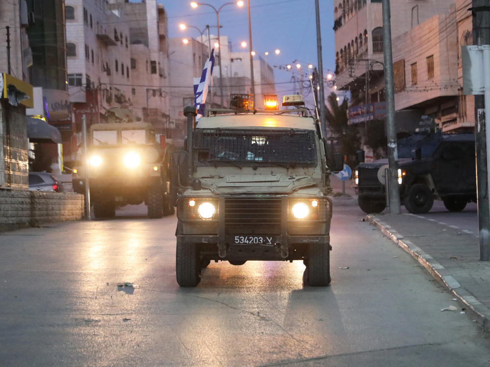 Israeli forces drive armored vehicles down a road during a raid in Hebron early on Jan. 21. The Israeli military says violence has surged in the West Bank since Oct. 7.
