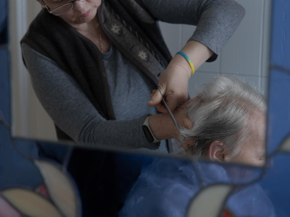 Caregiver Liliya Khodunay cuts Anna's hair in Anna's home in Milan, Italy, in February 2023.