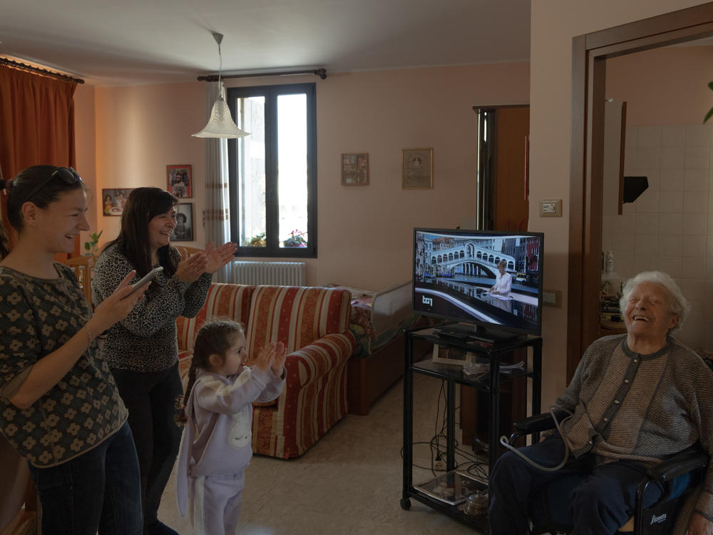 Khrystyna Mala, Lyubov Mala and Milana Dorosh applaud photographer Chiara Negrello's grandmother Lidia as she pushes her wheelchair by herself for the first time since returning home from the hospital in April 2022. Lidia was thin, breathing poorly, unable to feed herself and bedridden when she returned from the hospital. Lyubov helped Lidia improve so she could accomplish small tasks on her own.
