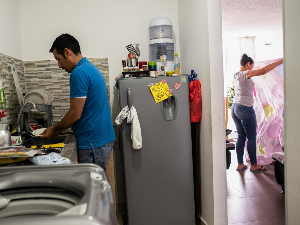 Ferley Sáenz and his wife, María Alejandra López, now divide up household chores. Here, Sáenz washes the dishes while López tidies up the living room.
