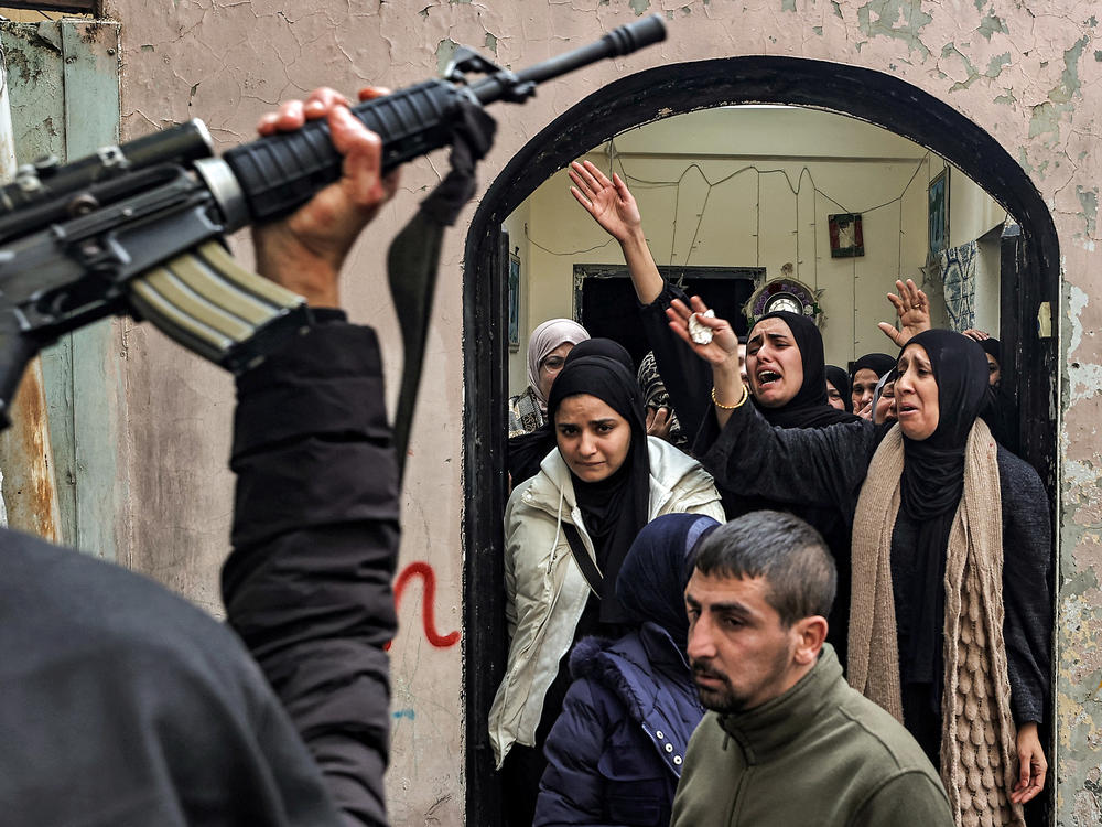 A man holds up an assault rifle as relatives mourn during the funeral of the two Ghazawi brothers, who were among three Palestinian men who were killed when undercover Israeli agents raided the Ibn Sina Hospital in the city of Jenin, in the occupied West Bank, on Jan. 30.