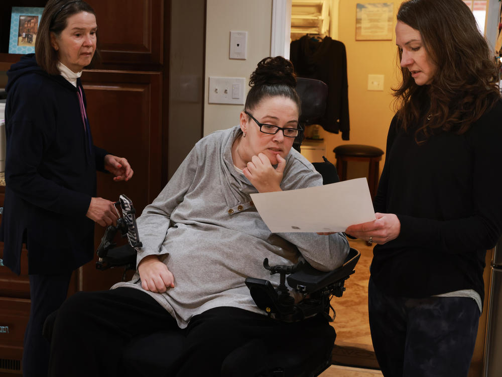 Hogan VanSickle gets help from her sister, Heather Hanson (right), and mother, Clara Brown, as they try to obtain fingerprints for her bar exam application, which is made challenging by the format and the limited mobility in her fingers.