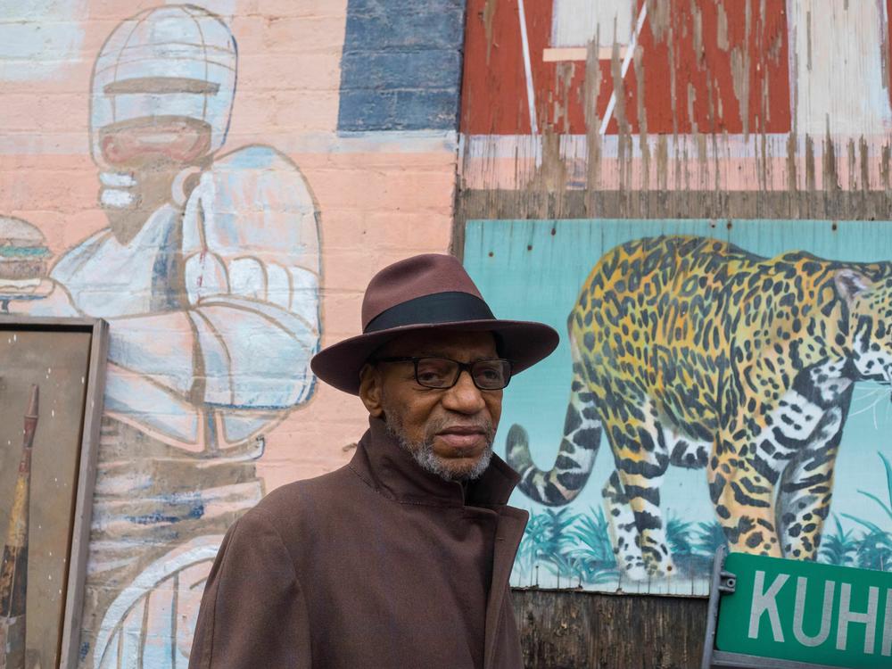 Muralist William Rankins Jr. stands in front of some of his murals in the Ollie's Trolley courtyard in Cincinnati. Ollie's is a restaurant.