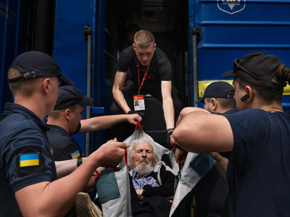 Eduard Skoryk (center) helps lift Viktor Nesterov onto an evacuation train leaving Toretsk, in eastern Ukraine, in May.