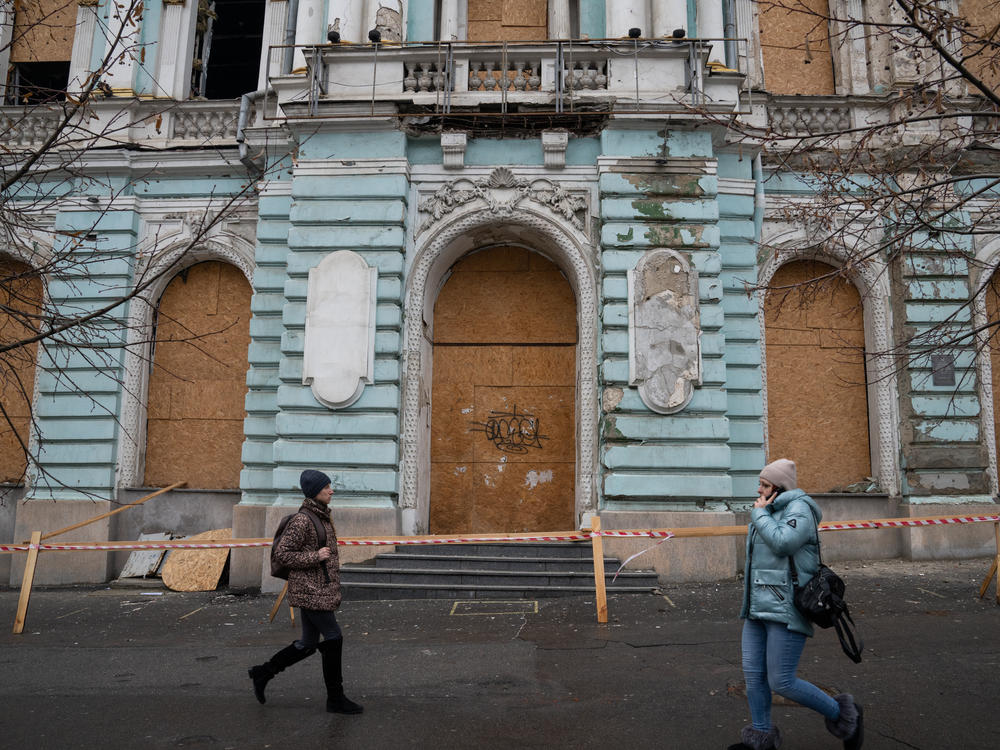 People walk in front of a historic building in Kharkiv that was damaged by a Russian strike.