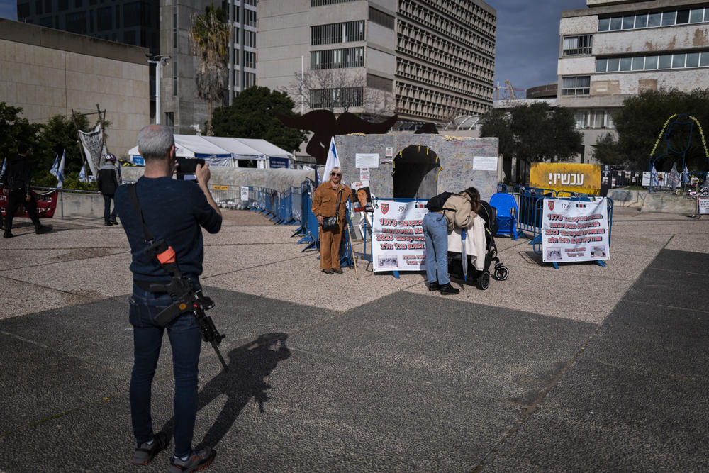 An armed Israeli man takes a photograph of a woman posing in front of a mock Hamas tunnel in what's known as Hostage Square in Tel Aviv, a round-the-clock encampment for those seeking the return of Israelis held by Hamas in Gaza.