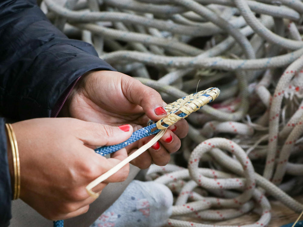 A craftswoman interweaves discarded climbing rope with Moonj, a traditionally harvested harvested wild grass, to make a decorative item.