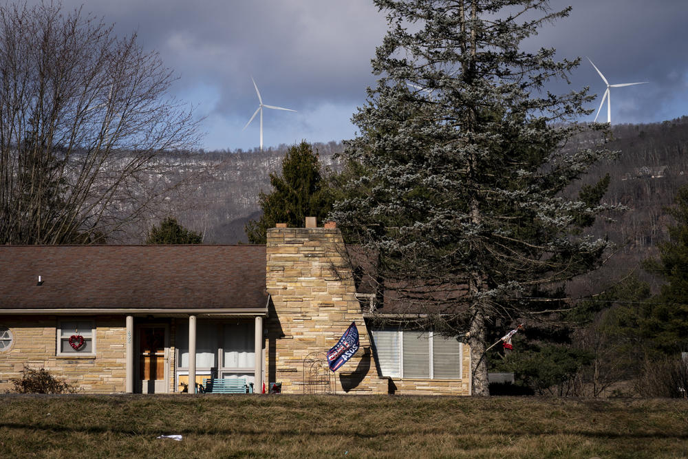 Wind turbines turn in the background as a flag that reads 