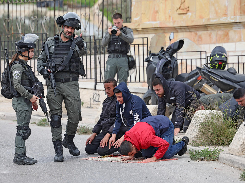 Israeli security forces stand guard as Palestinians observe their noon prayers on a street in east Jerusalem on Friday, Feb. 23.