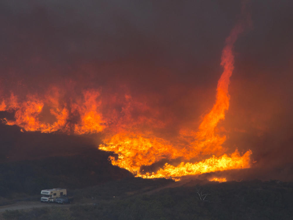 A fire tornado forms near cars parked on a country road at the Blue Cut Fire in 2016 near Wrightwood, California. Climate change is causing longer and more active fire seasons, according to the National Oceanic and Atmospheric Administration.